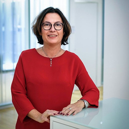 Porträt von Wiebke Küpper, die in einem roten Kleid an einem weißen Schrank lehnt. 