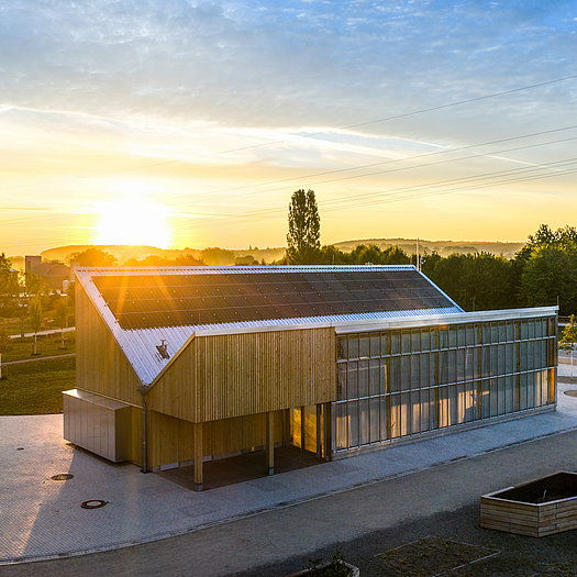 Holzgebäude des Klimapavillons mit Photovoltaikanlage auf dem Dach bei tief stehender Sonne.