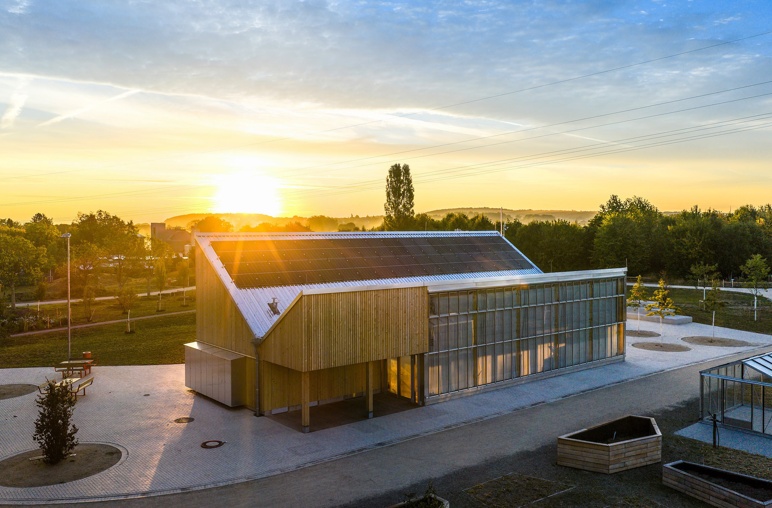 Holzgebäude des Klimapavillons mit Photovoltaikanlage auf dem Dach bei tief stehender Sonne.
