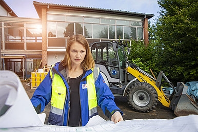Die Projektleiterin steht vor der Baustelle des Ausbildungszentrums der Bundespolizei in der Alheimer-Kaserne in Rothenburg an der Fulda und schaut sich die Baupläne an. 